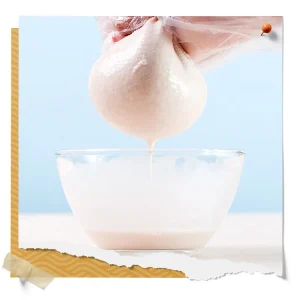 Fresh mozzarella cheese curd draining in cheesecloth over a glass bowl during the cheese-making process.