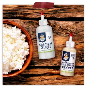 Calcium chloride and double-strength liquid microbial rennet bottles beside a bowl of fresh cheese curds on a rustic wooden surface.