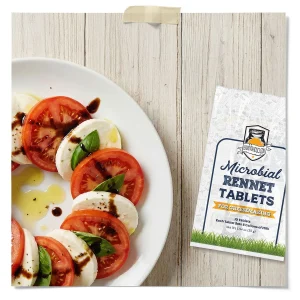 Caprese salad with fresh mozzarella, sliced tomatoes, basil, olive oil, and balsamic glaze beside Fermentaholics microbial rennet tablets for cheesemaking.